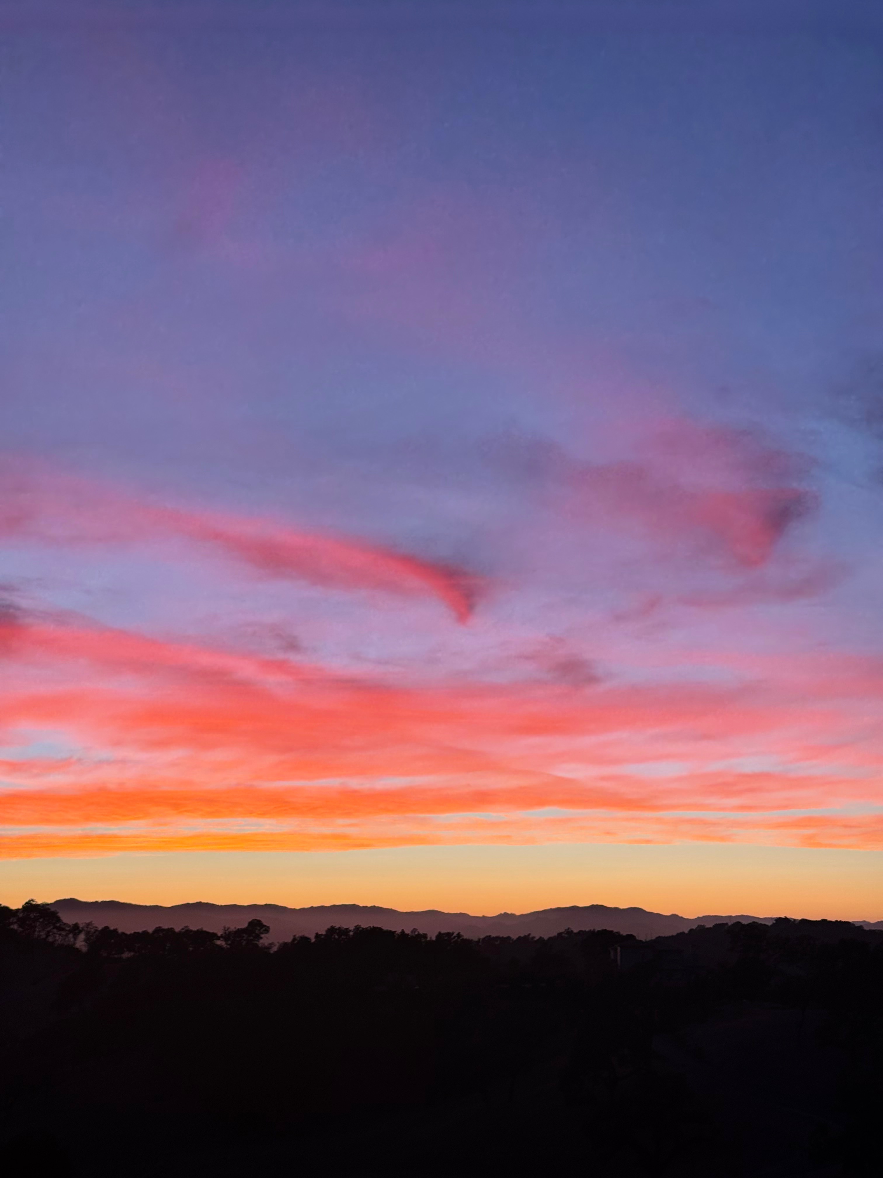 Pink and orange sunset clouds above a dark mountain horizon